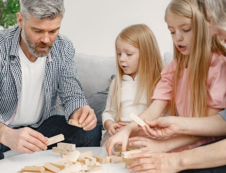 Four family members of different ages engage with toy blocks on a table indoors.