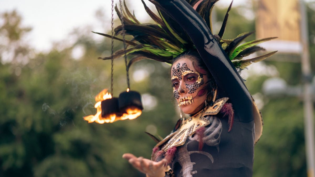 A performer in Catrina costume and makeup spins fire outdoors in Mexico City.
